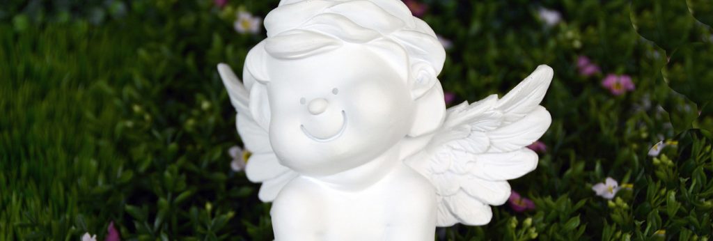 Ein weißes Friedensengelchen aus Porzellan sitzt auf einer Blumenwiese